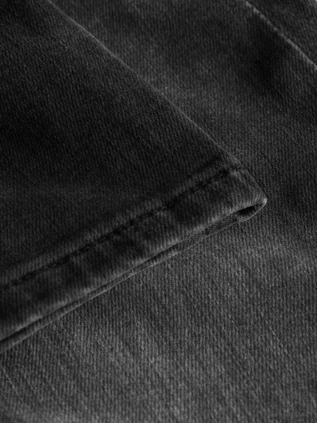 Close-up of Rey Thor Jeans by GABBA in dark gray denim wash, featuring a textured diagonal weave pattern. The versatile fabric is folded at the edge with visible stitching along the hemline, offering a laid-back look.