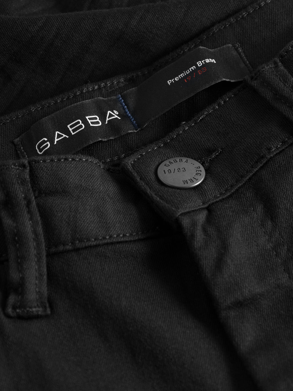 Close-up of GABBAs Jones K1911 Black Jeans showcasing the brand label inside the waistband. The metallic button embossed with Gabba 18/20 is partially covered by a flap. The slim fit pairs perfectly with the textured, slightly faded black denim.