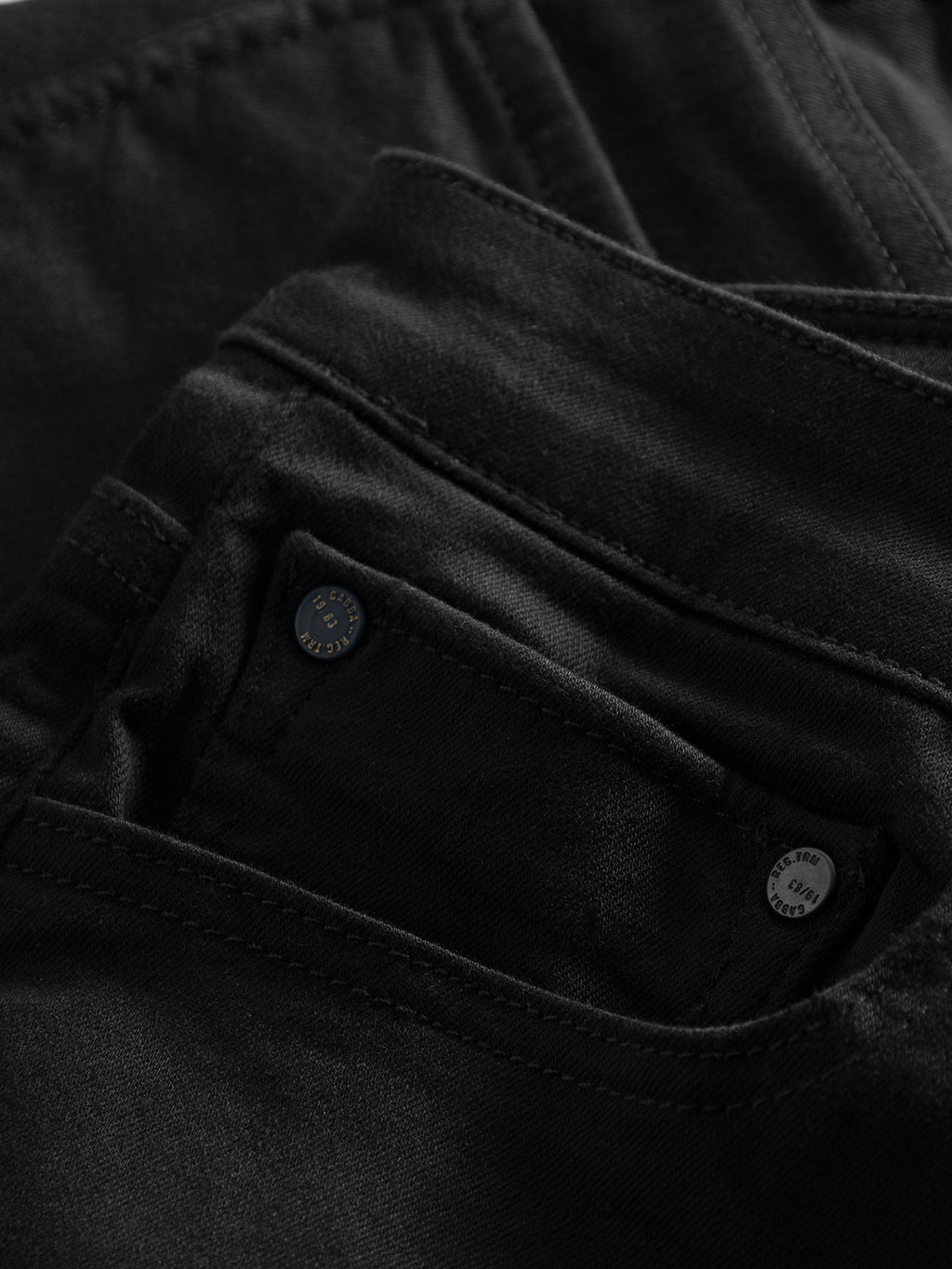 Close-up of the pocket and stitching on GABBAs Jones K1911 Black Jeans. The super-stretch fabric enhances the slim silhouette with visible texture. A metal button on the pocket features engraved text, partially showing the word BUTTON.