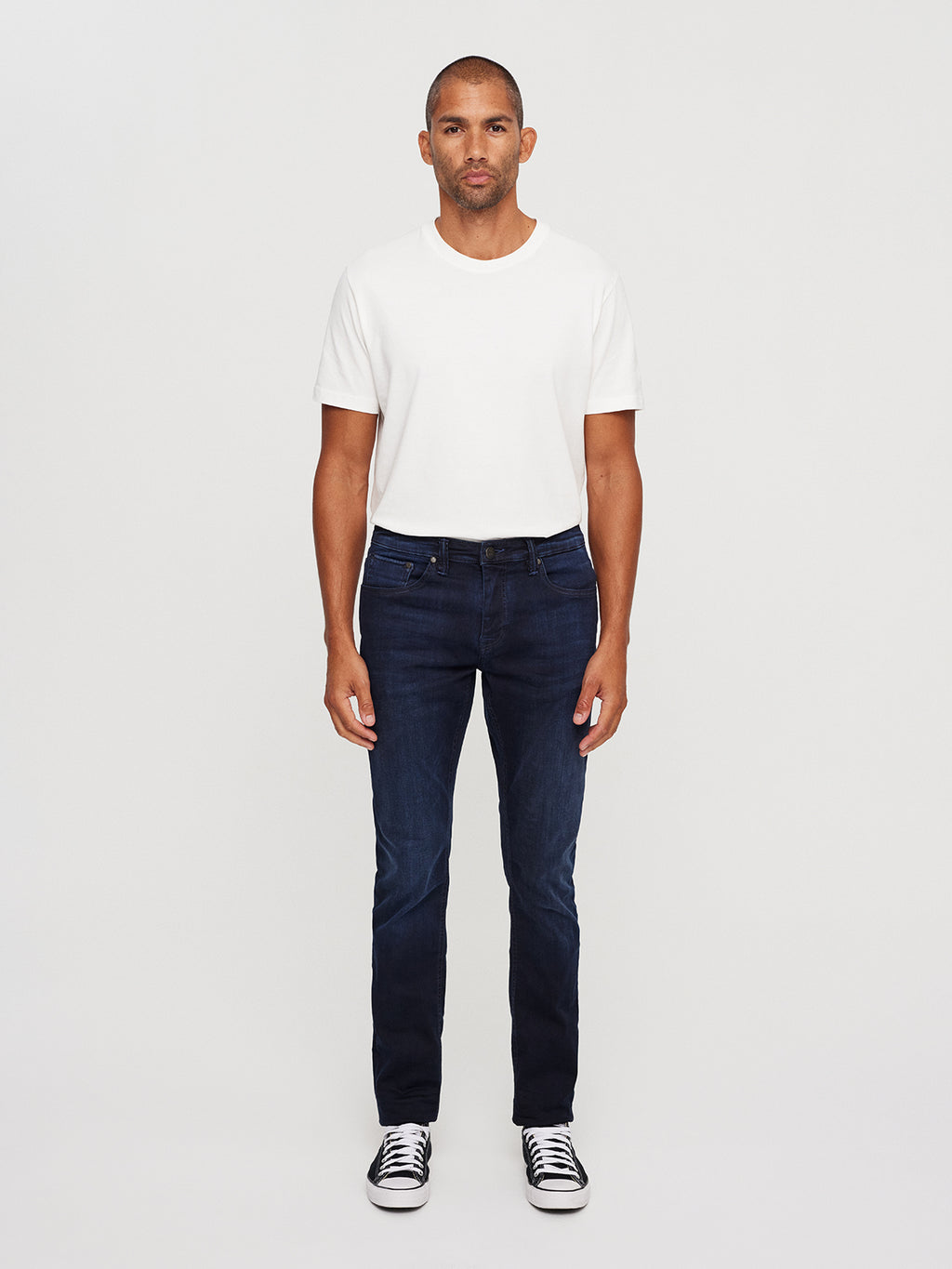 A man stands facing forward, wearing a plain white T-shirt and GABBAs Jones K2291 - Denim wash jeans, featuring super-stretch fabric in a dark blue slim silhouette. His black sneakers with white soles complete the look against a plain white background.