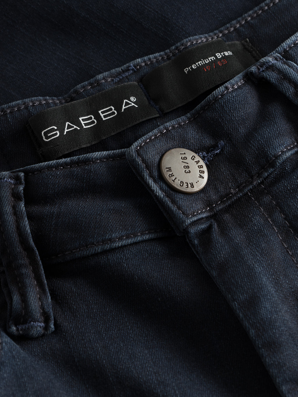 Close-up of Jones K2291 - Denim wash by GABBA, detailed with a metal button engraved GABBA and a black label with GABBA in white text. The slim silhouette jeans have reinforced pockets, display Premium Brand and 1969, and feature visible belt loops on the waistband.