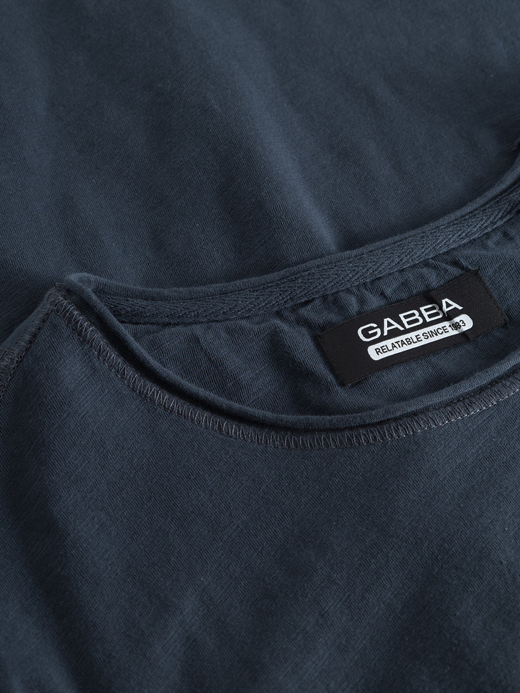 Close-up of the Konrad Slub S/S Tee - Navy collar featuring a GABBA Reliable since -85 label. The fabric looks soft and textured, ideal for comfort.