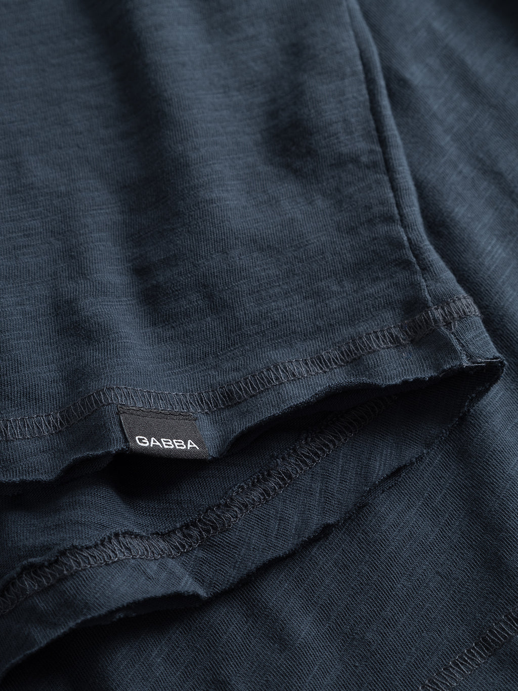 A close-up of the navy Konrad Slub S/S Tee by GABBA shows textured fabric, stitch detailing, and layering. This regular fit tee offers comfort and is perfect for those valuing craftsmanship in their basic collection.