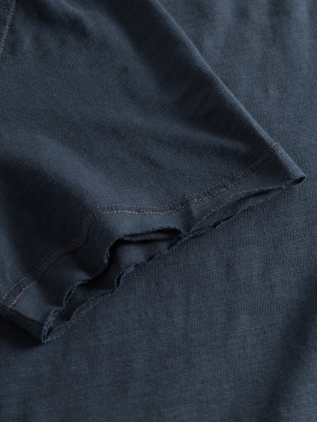 Close-up of a Konrad Slub S/S Tee - Navy by GABBA, highlighting its fine stitching and soft texture against a matching fabric background. The image showcases the tees material and construction details for comfort and regular fit.