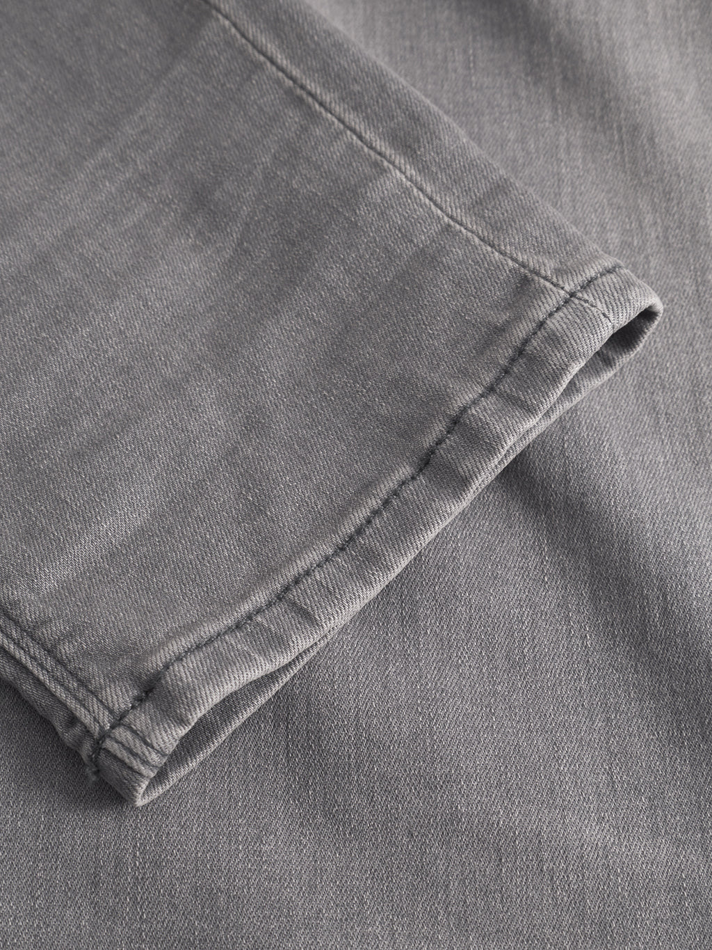 A close-up of the hem on GABBA’s Rey K3454 - Denim wash slim fit jeans, showing off texture and stitching, with the pant leg laid flat on a matching gray surface for a relaxed look.