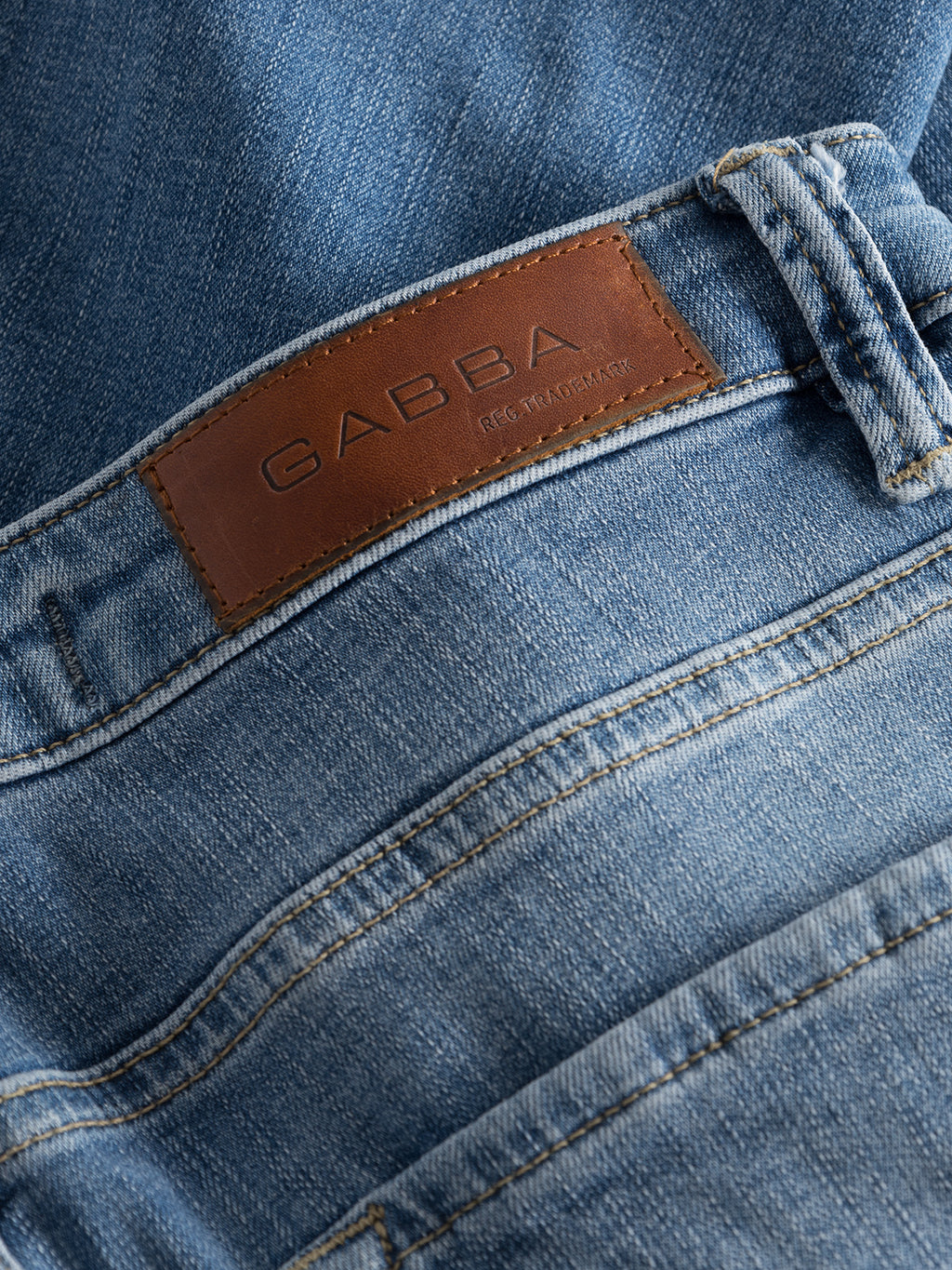 Close-up of Jones K2615 Lt. denim wash jeans, showing a brown leather patch embossed with GABBA on the waistband. Made from super-stretch fabric, they feature visible stitching and belt loops, providing a sleek slim silhouette in light blue denim.