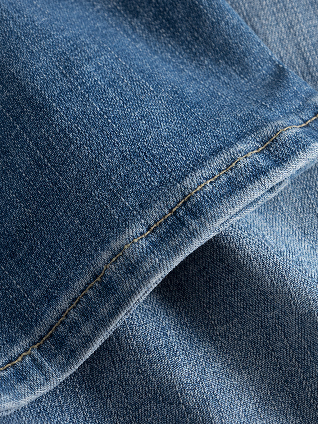 A close-up of the Jones K2615 Lt. - Denim wash by GABBA reveals the detailed texture and stitching of blue denim fabric. The focus on the seam highlights its weave and color transitions from light to dark blue, showcasing a super-stretch material crafted for a slim silhouette.
