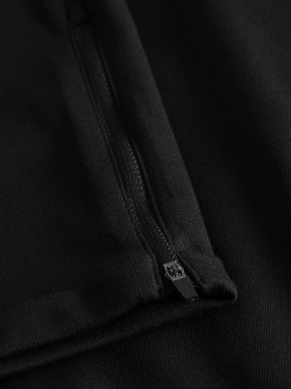 A close-up of the Pisa Jersey Pant - Black by GABBA shows a subtle zipper blending into the smooth, textured high-stretch fabric. This piece embodies a sleek metropolitan look, ideal for those who appreciate understated sophistication.