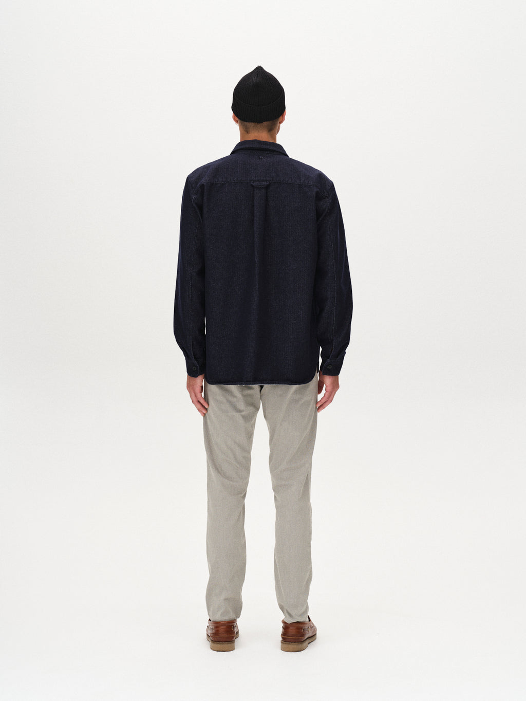 A person wearing a black beanie, a dark long-sleeve shirt, Gabba Paul K3280 Dale Chino - Birch pants, and brown shoes stands facing away against a plain white background.