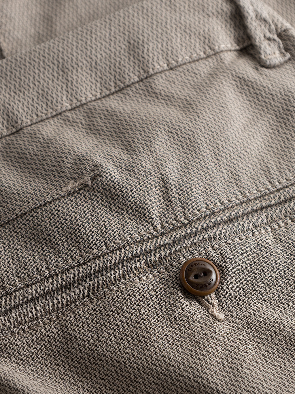 Close-up of beige textured fabric from the Paul K3280 Dale Chino - Humus by GABBA, featuring French pockets and a buttoned stitched seam. The fabric has a subtle woven pattern, with a small, round button sewn onto these slim chino pants.
