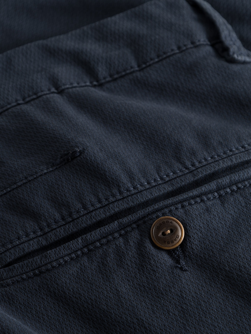 Close-up of GABBAs Paul K3280 Dale Chino in navy fabric, featuring a small brown button with an engraved design and a zipper. The slightly ribbed texture adds depth, while double-paspel back pockets complement the closed zipper with partially visible teeth.