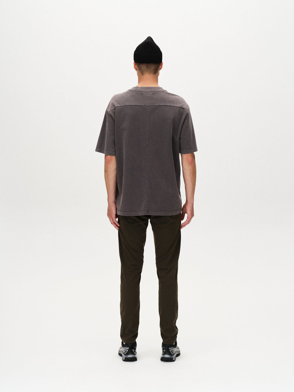 A person wearing a black beanie, short-sleeved gray shirt, GABBA Paul K3280 Dale Chino in Army, and black sneakers stands facing away against a plain white background.