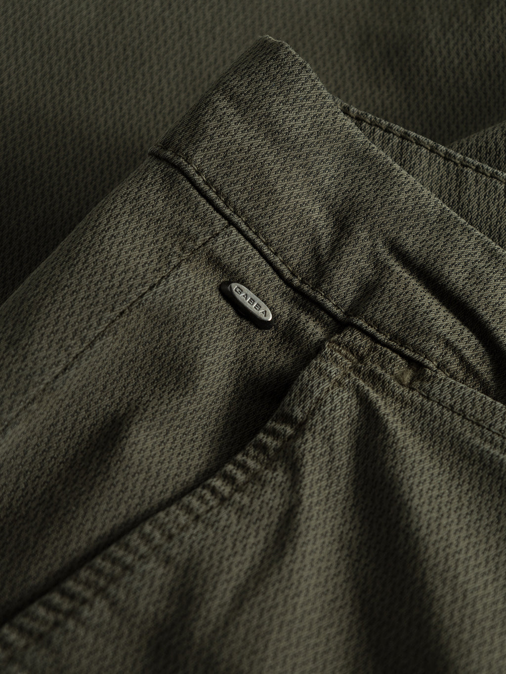 The close-up of the GABBA Paul K3280 Dale Chino - Army shows the olive green slim fit, subtle texture, waistband with a small silver tag, and detailed stitching. The fabric looks soft with French pockets offering a relaxed yet structured design.