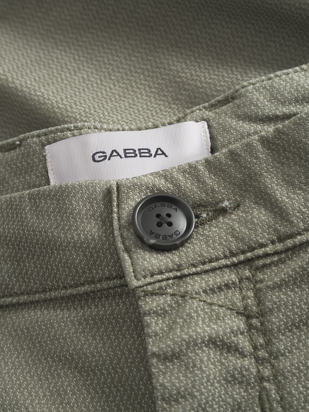 Close-up of Paul K3280 Dale Chino in olive green by Gabba, showing textured fabric, branded Gabba-engraved buttons, and a white label inside the waistband with Gabba in black text.