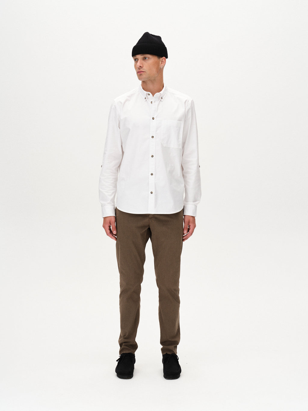 A person in a black beanie, white button-up shirt, Gabba Paul K3280 Dale Chino - Crocodile pants, and black shoes stands against a plain white background, looking slightly to the side.