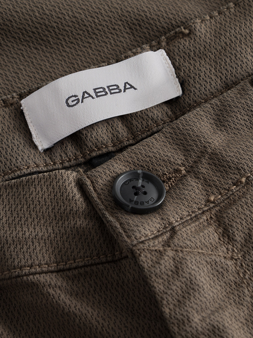 Close-up of Gabba Paul K3280 Dale Chino in Crocodile: brown textured slim-fit pant with French pockets, visible stitching, a black button engraved with Gabba, and a white label showing the brand name.