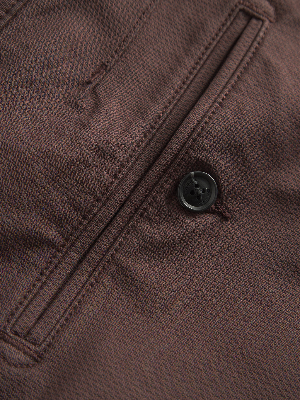 Close-up of Paul K3280 Dale Chino in Burnt Purple by Gabba, showcasing brown textured fabric with a branded black button next to a vertical seam typical of French pockets, possibly part of a jacket or coat.