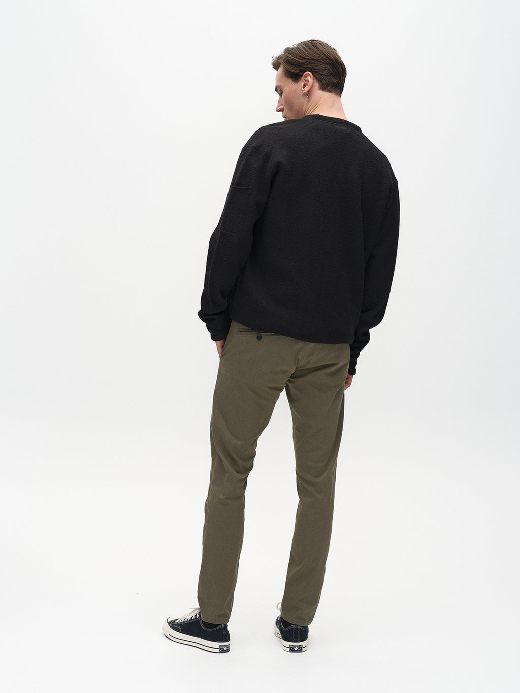 Someone is dressed in a black sweater and Gabbas Paul K3280 Dale Chino pants in Deep Lichen Green, paired with black sneakers, standing against a plain white background.