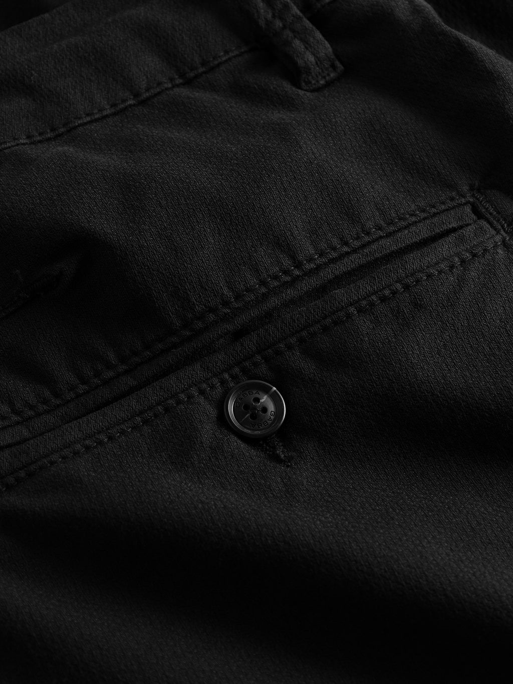 Close-up of the textured black fabric from Paul K3280 Dale Chino by GABBA, highlighting a back pocket with branded buttons. Visible stitching around the French pockets reflects the typical design of slim chino pants.