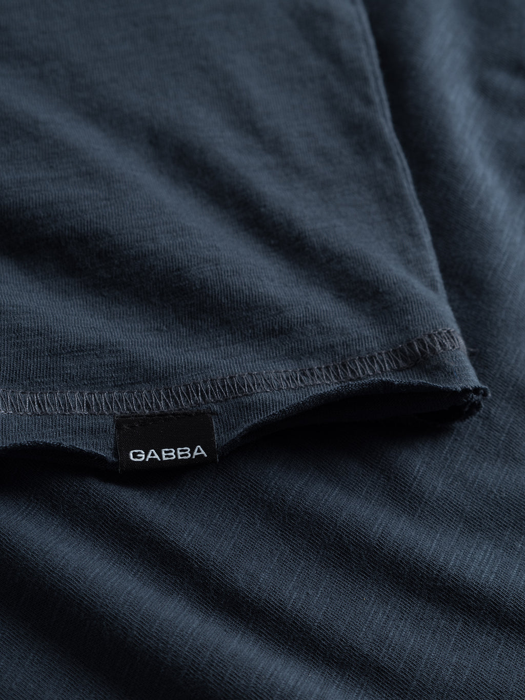 Close-up of the Konrad Straight Slub Tee by GABBA in navy. The soft, dark fabric, similar to cotton slub yarn, features a sewn label and a slight edge fold, enhancing its casual look.