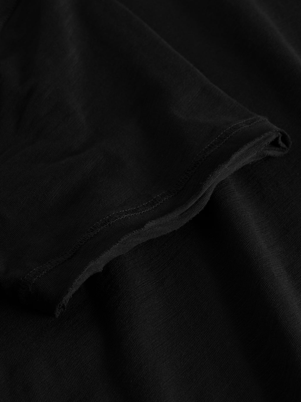 Close-up of the GABBA Konrad Straight Slub Tee in black, focusing on a short sleeve edge. The soft, smooth texture reveals detailed stitching along the hemline, with lighting enhancing the unique charm of cotton slub yarn.