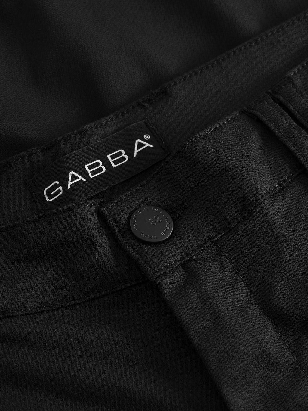 Close-up of Pisa Cargo K3280 Dale Pants by GABBA in black, showing a visible GABBA label, black waistband button, slim tapered fit, super stretchy fabric, and detailed stitching.