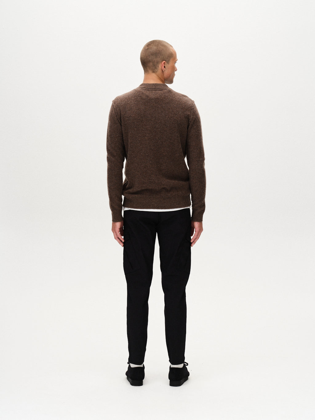 A person with a shaved head, wearing a brown sweater and GABBA Pisa Cargo K3280 Dale Pants in black, paired with black shoes, stands facing away from the camera against a plain white background.