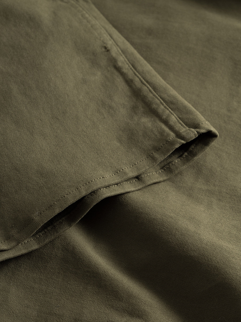 Close-up of the army olive green fabric from GABBAs Topper LS Shirt, showcasing visible edge stitching on this smooth yet slightly textured material, suggestive of a garment featuring chest pockets or button closures.