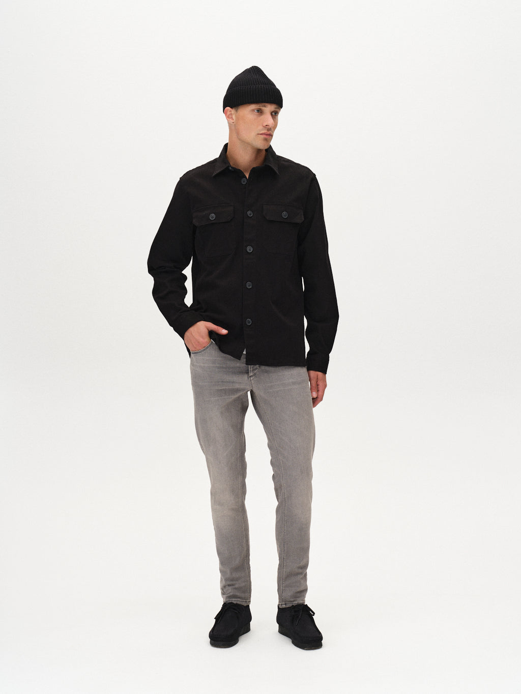 A man wears the GABBA Topper LS Shirt in black, paired with light grey jeans and black shoes, standing against a plain white background and looking slightly to his left.