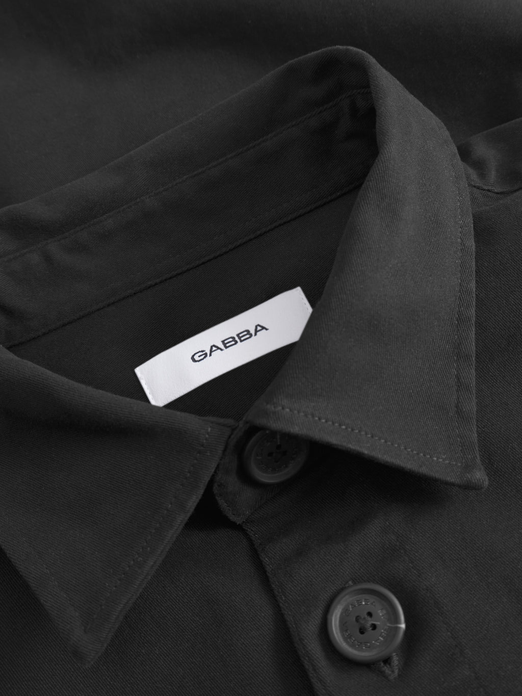 Close-up of the GABBA Topper LS Shirt in black, featuring a collared design with black buttons and a white brand label inside the collar—ideal for layering.