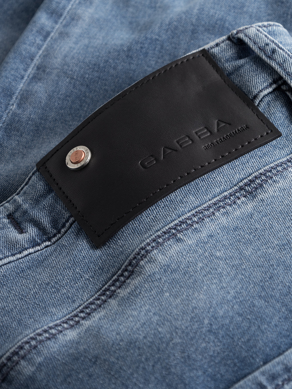 Close-up of Rey K3866 TENCEL™ jeans by GABBA in blue denim wash, featuring a black leather patch with embossed text and a silver button. These slim-fit jeans have textured denim and a light wash finish, ideal for a relaxed style.