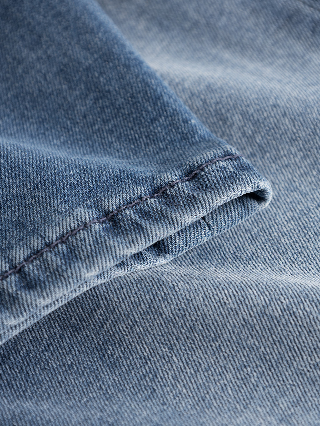 A close-up of Rey K3866 TENCEL™ jeans from GABBA reveals the textured blue denim weave and stitching details on a folded edge, ideal for a laid-back look. The classic hue with subtle variations highlights the natural texture synonymous with these jeans.