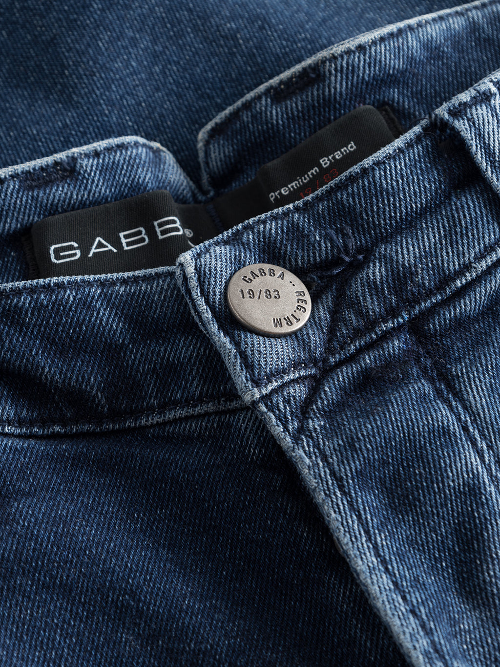 Close-up of Alex K3868 Jeans - Denim wash by GABBA, featuring a metal button engraved with GABBA, 19/83, and W34. With worker-cut waistbands and trendy look, the GABBA Premium Brand label ensures quality. Visible stitching and rich texture cater to casual style enthusiasts.