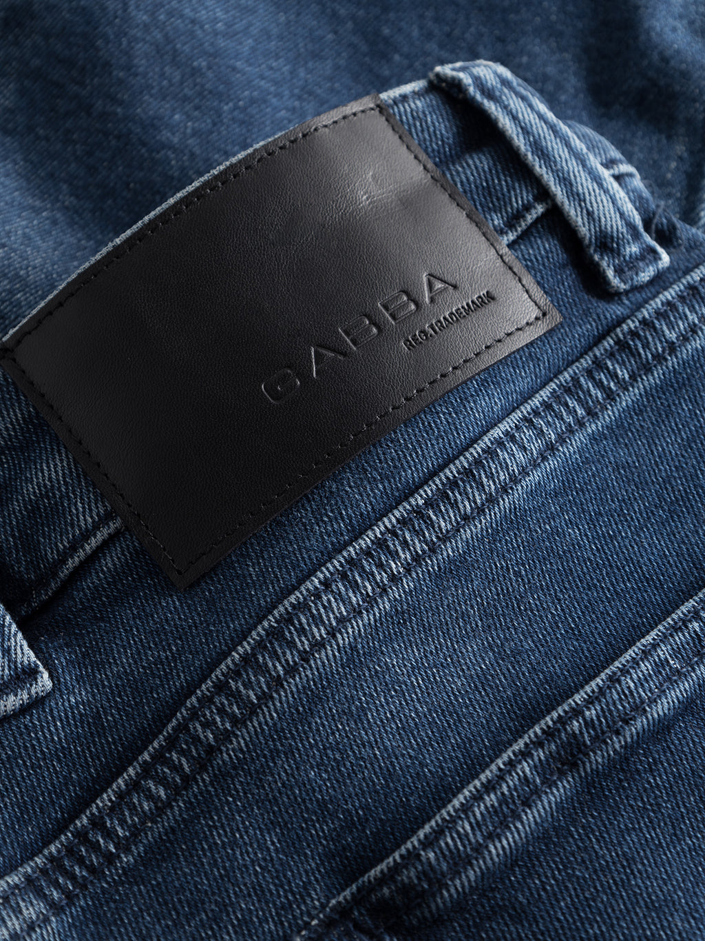 A close-up of GABBAs Alex K3868 Jeans in blue denim wash, featuring a black leather patch on the waistband embossed with GABBA JEANS. The worker-cut waistband emphasizes trend-focused style, visible stitching, and a classic pocket design enhancing their casual appeal.