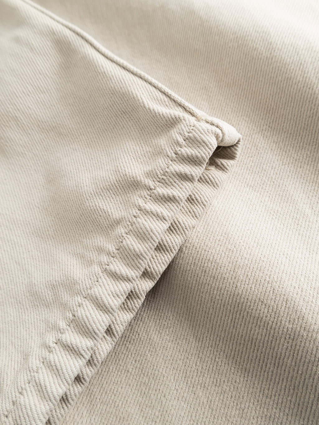 Close-up of the hem and seam of GABBAs Zem K3992 Jeans in beige, featuring visible stitching with smooth texture and slight ribbing. The fabric is slightly folded at the corner, echoing precise sewing detail reminiscent of an Urban 90s vibe.