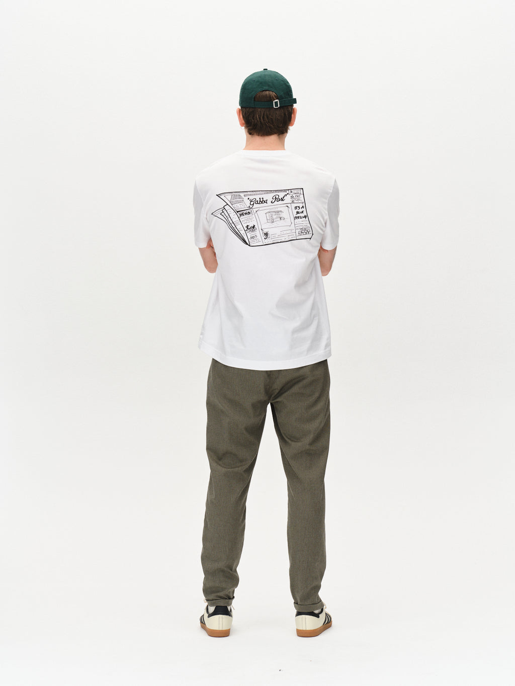 A person stands facing away in Gabba Pisa Domo Pants - SS25Army, styled with a green cap, graphic pizza box T-shirt, and beige shoes, embodying easy metro style against a white background.