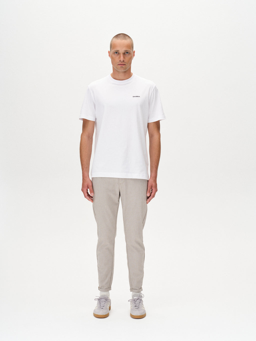 A man in a plain white t-shirt and Gabba Pisa Domo Pants – Coriander, made from high-stretch cotton-blend, stands against a white background with light sneakers and a neutral expression, his arms by his sides for a modern metro look.