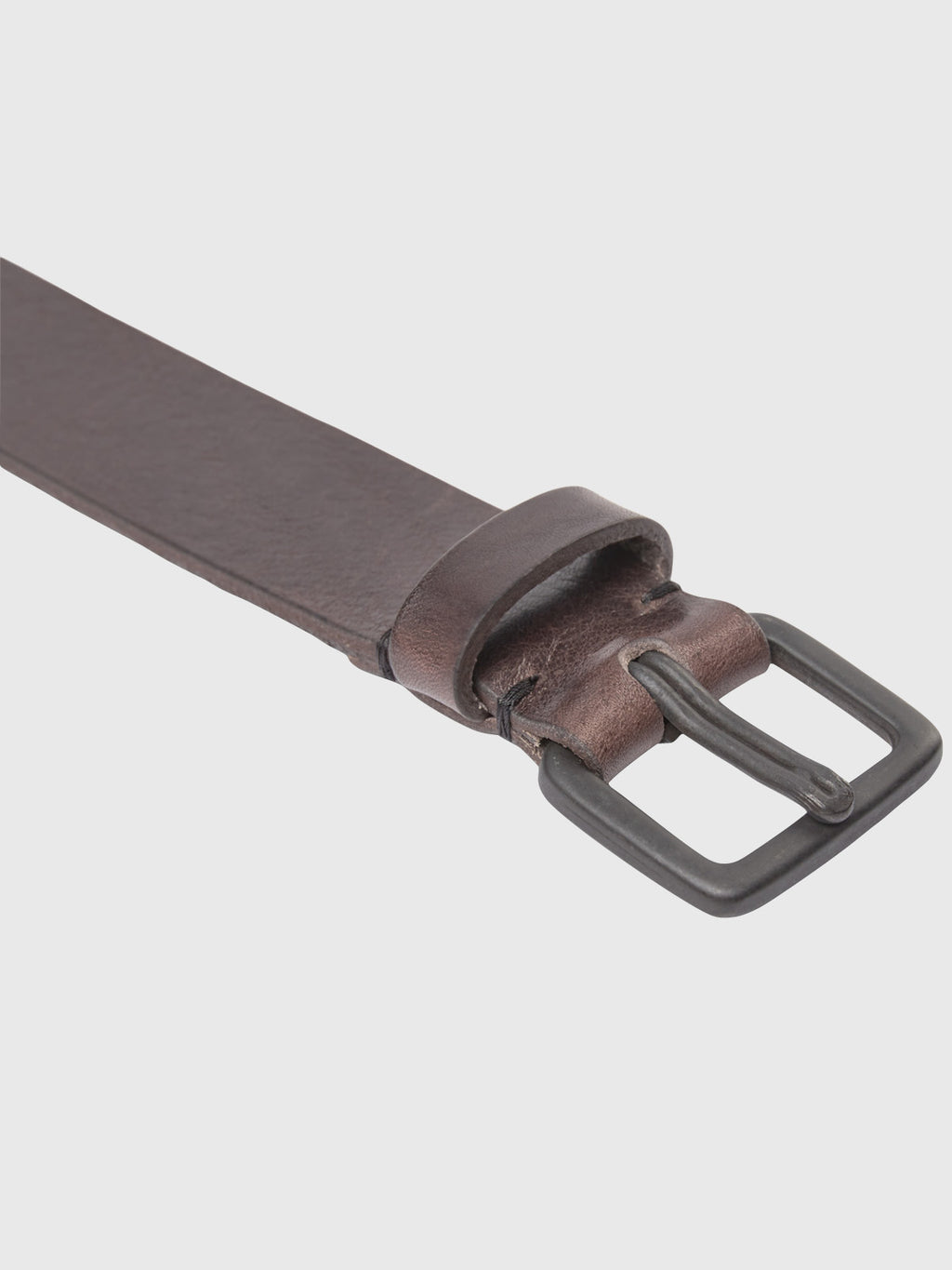 A light gray background showcases the Okay Belt - Brown from GABBA, featuring a minimalist design. This dark brown leather belt includes a rectangular black metal buckle and leather loop, crafted from premium materials for a smooth texture.