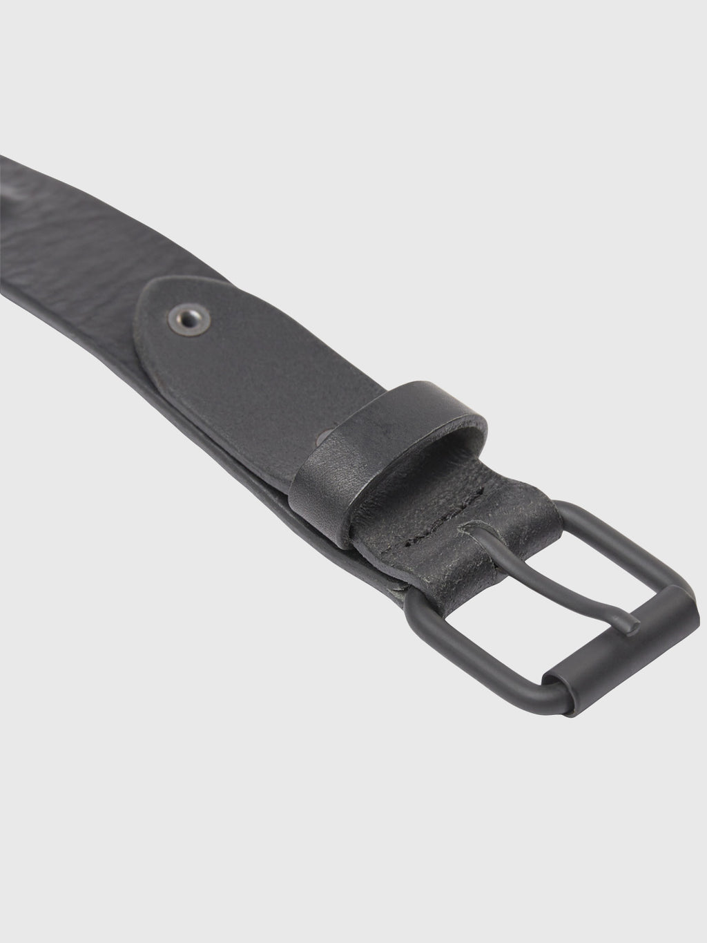 A close-up of the Okay Point Belt by GABBA, featuring its classic black leather laid flat, highlights the rectangular metal buckle and a single row of holes. Crafted from premium leather, it showcases smooth texture and visible stitching against a light gray background.