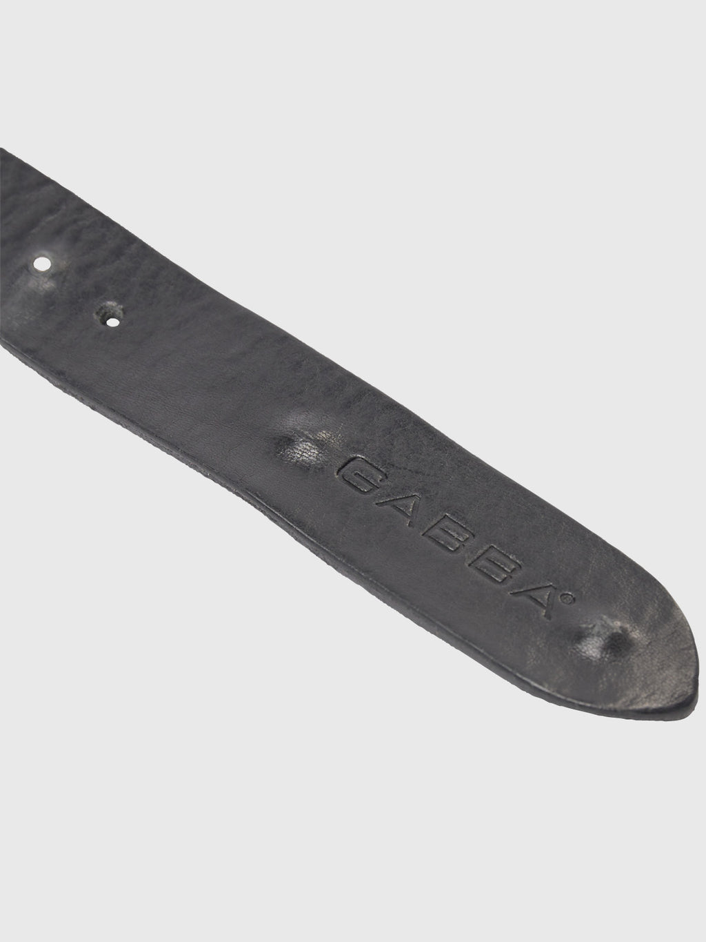 Close-up of the Okay Point Belt - Black by GABBA, featuring a classic leather tip with three adjustment holes. The embossed GABBA brand signifies premium quality. Slightly curved, it showcases the rich leather texture against a light gray background.