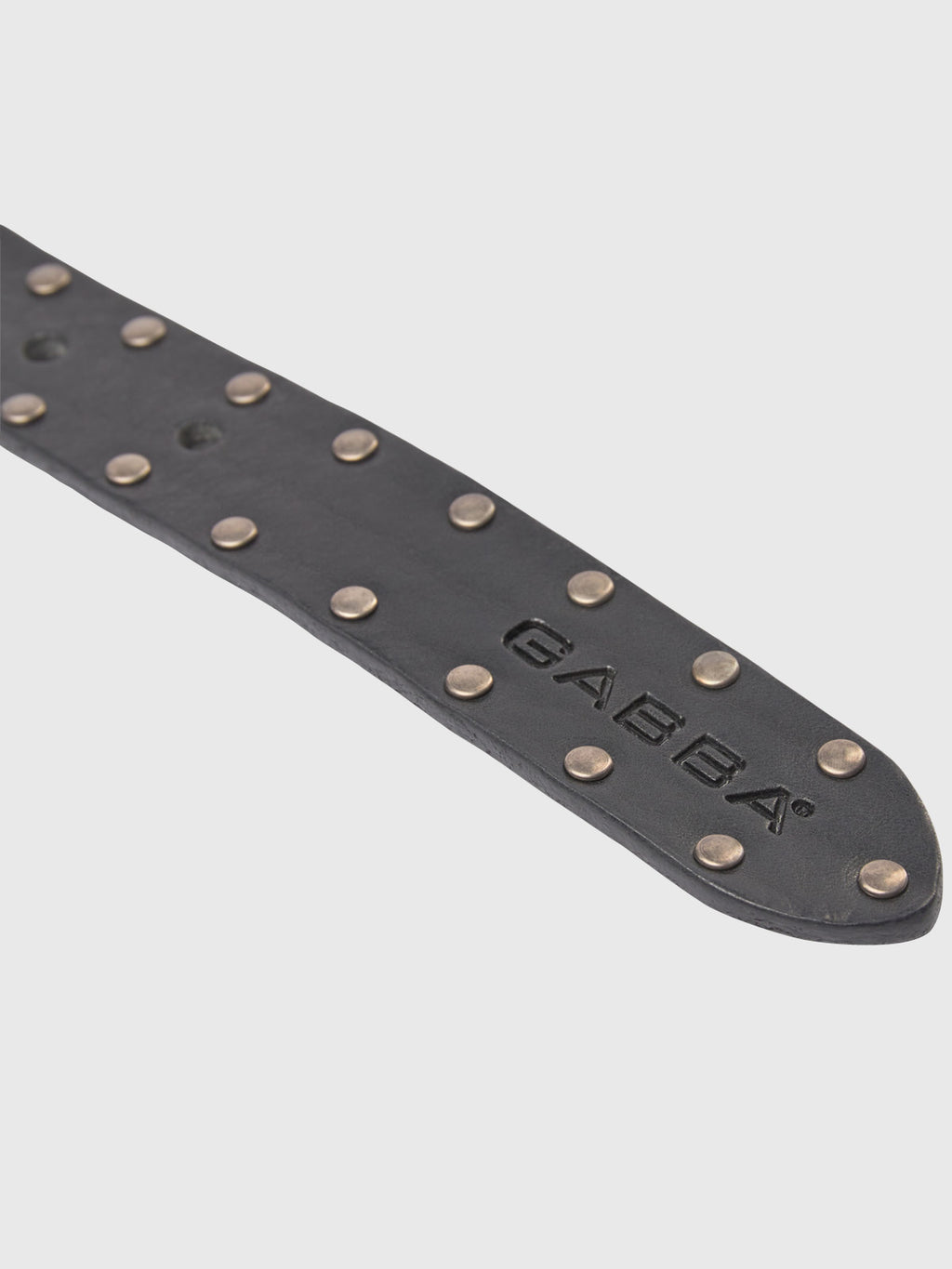Close-up of the Okay Stud Belt by GABBA, a black leather belt with a raw finish, featuring metal studs and GABBA embossed on it against a plain light gray background.