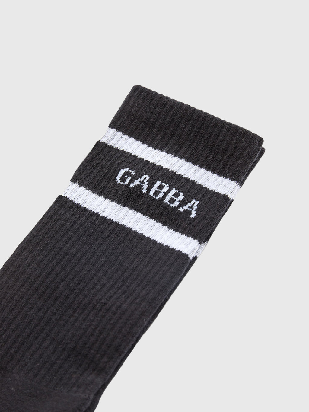 A close-up of a Loris sock by Gabba highlights its comfortable fit, featuring two white stripes near the top and GABBA in bold letters below. Diagonally set against a light gray background, this stylish black sock is ideal for daily wear.