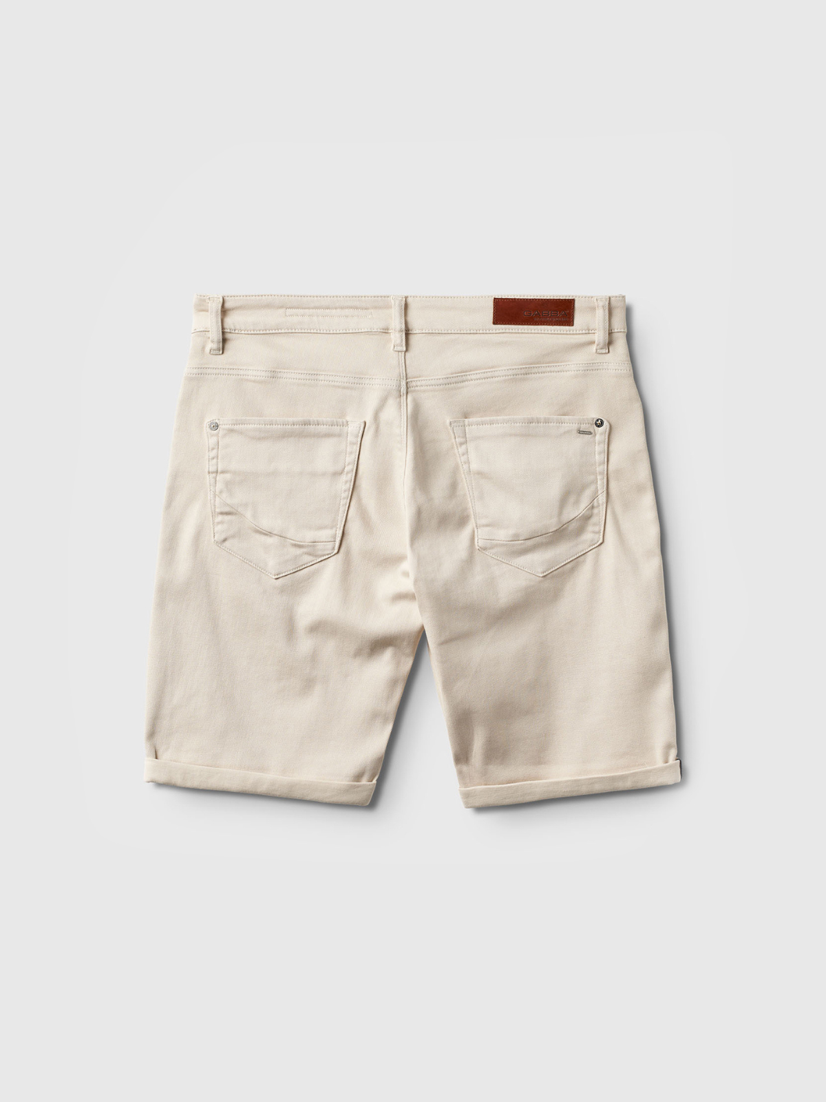 Back view of Gabba Jason K3995 SANZA Shorts in Birch—beige, knee-length denim with two back pockets, belt loops, a brown leather patch on the waistband, and super stretch fabric, shown against a light gray background.