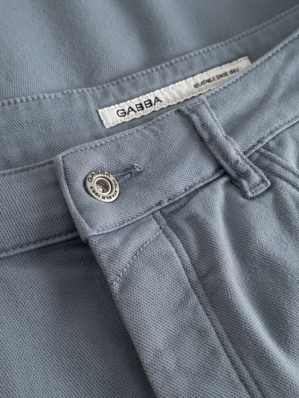 Close-up of Gabba GABjason K3995 SANZA Shorts in Denim Blue, showcasing a metallic button, belt loop, and white Gabba label on the waistband. Crafted from super stretch fabric for comfort.