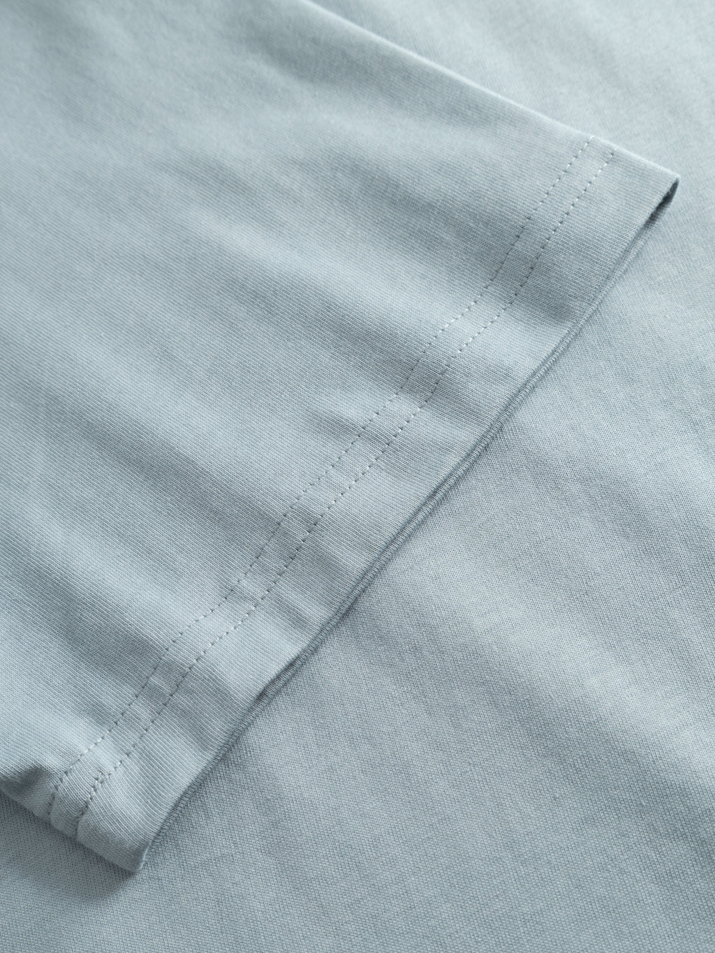 Close-up of the Gabba GABdune Logo SS GOTS t-shirt sleeve in light blue, showcasing its organic cotton fabric texture and tidy double stitching along the hem.