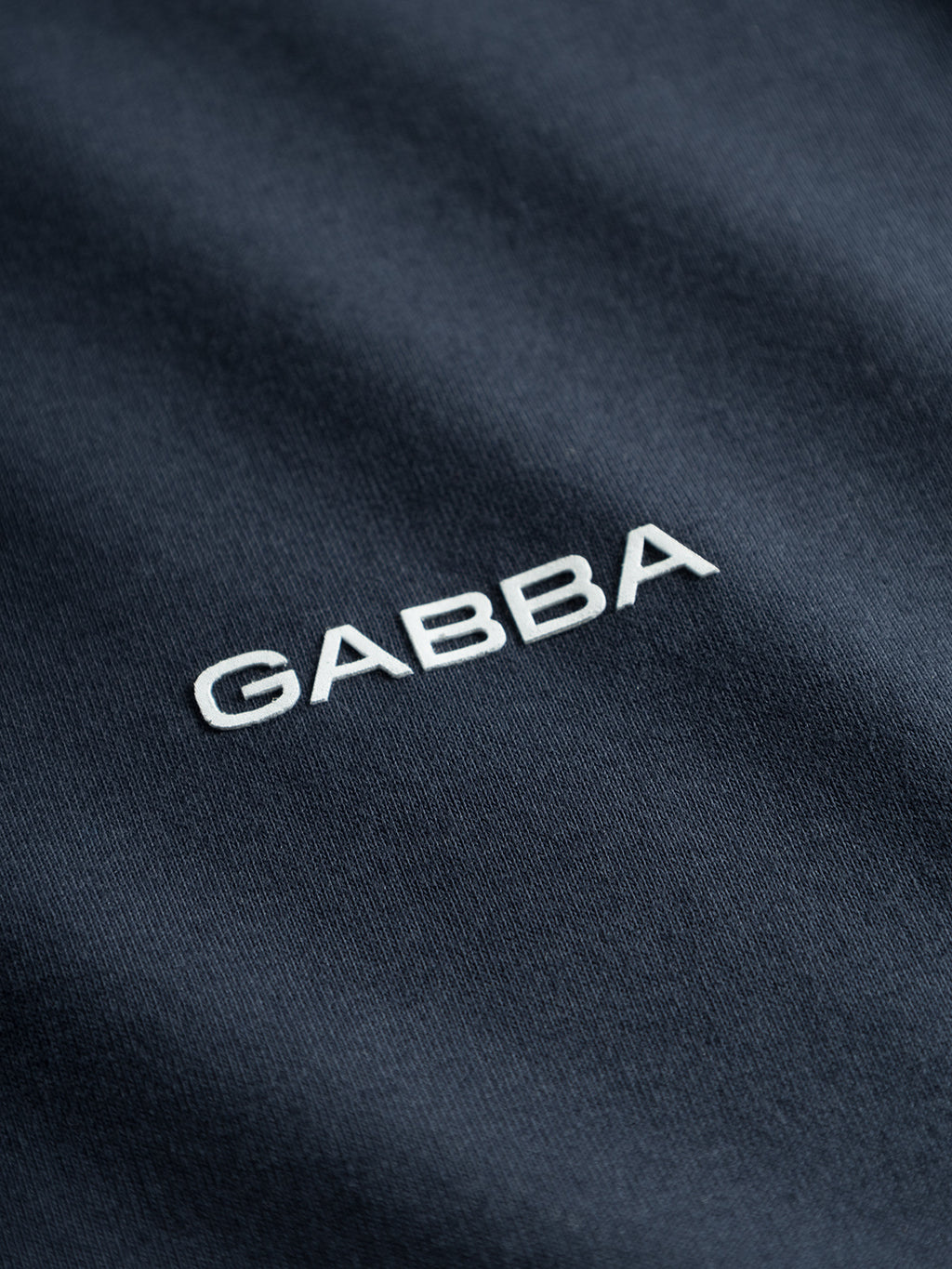 Close-up of dark GOTS-certified organic cotton from Gabba’s Dune Logo SS GOTS - Total Eclipse, featuring “GABBA” boldly embroidered in white at the center—perfect for a basic t-shirt.