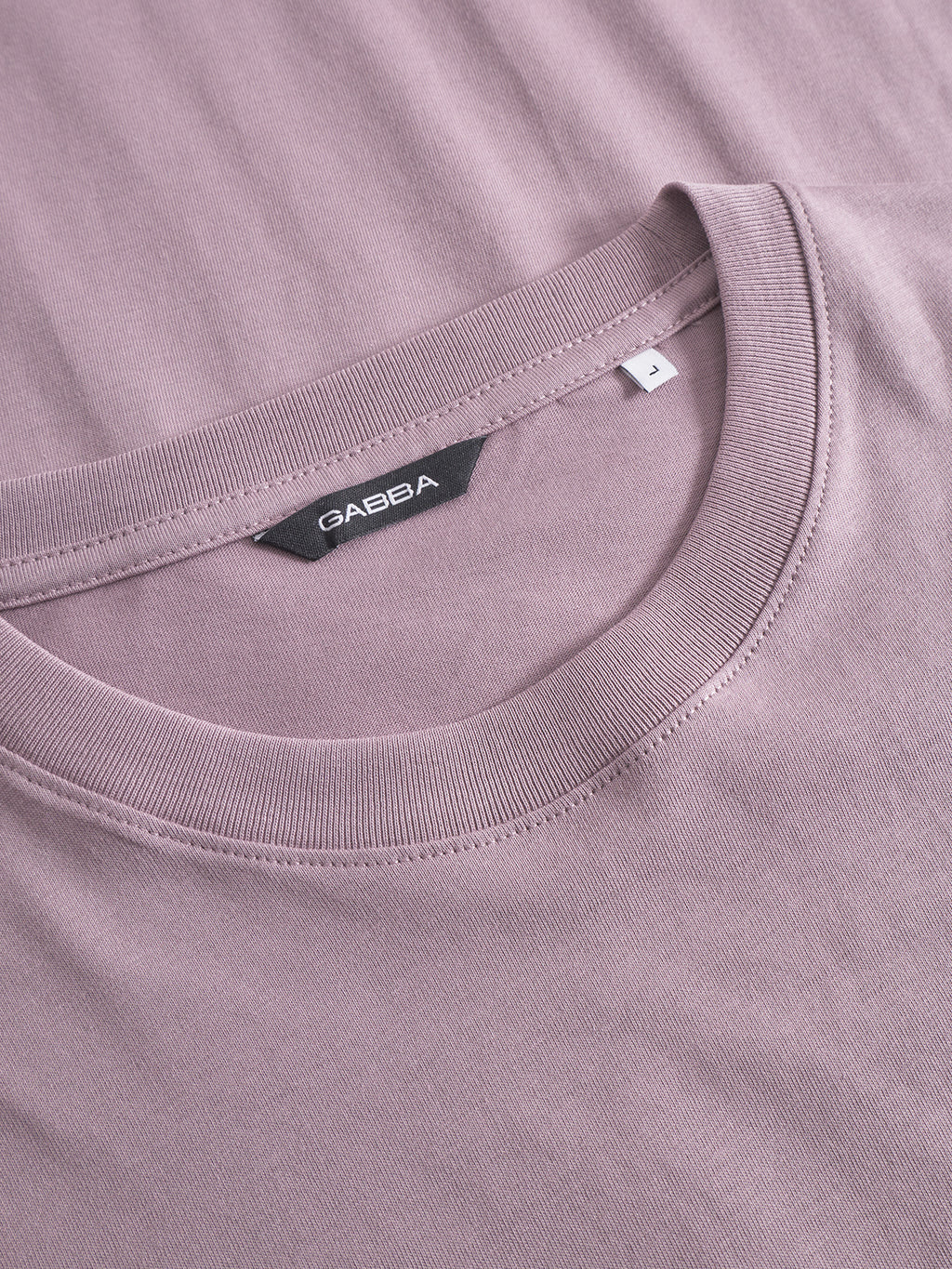 Close-up of the Dune Logo SS GOTS t-shirt by Gabba in Dust Purple, featuring a crew neckline, fine stitching, and a black Gabba label with a white L size tag. Made from organic cotton.