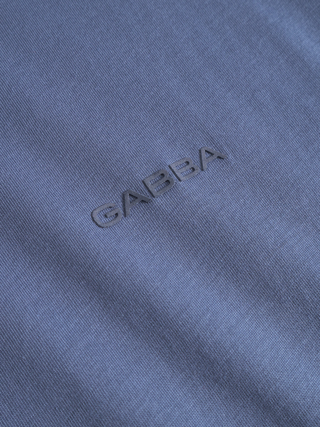 Close-up of vintage indigo fabric from the Gabba Dune Logo SS GOTS t-shirt, featuring the word Gabba subtly embroidered in matching blue thread for a raised texture.