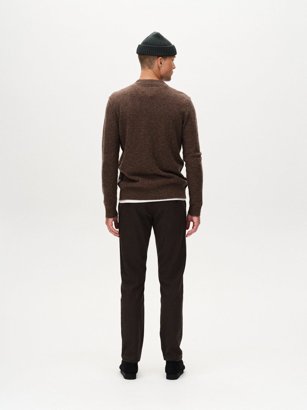 A man faces away from the camera, wearing a green beanie, black shoes, and Gabbas Paul Domo - Dk. Brown slim chino pants with French pockets against a plain white background.