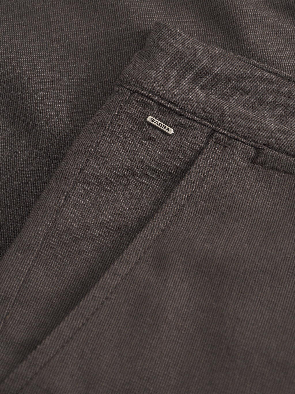 Close-up of Paul Domo - Dk. Brown corduroy slim chino pant by Gabba, featuring a front French pocket, belt loop, branded buttons, and a small metallic Gabba label above the pocket.